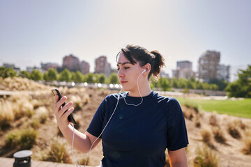  A beautiful white woman with brown hair and a sports outfit sends a message by cell phone to one of her friends