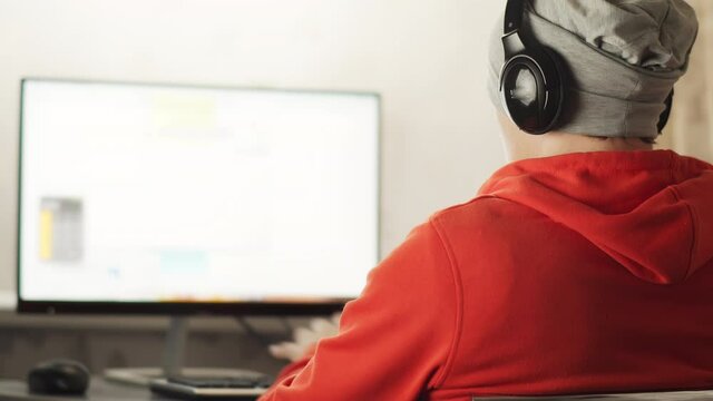 A programmer in a works in a home office in the evening sitting at a monitor screen, develops sites