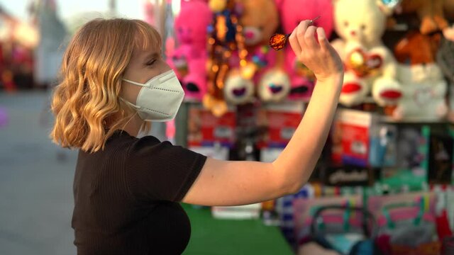 Chica rubia espa&ntilde;ola jugando a explotar globos de colores en puesto de feria