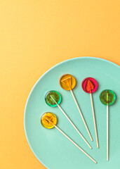 Sugar-free fruit lollipops 
laid out on a green plate on a minimalistic background in pastel yellow color. Healthy sweetness 
with dry fruit inside