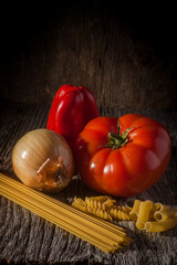 Food Ingredients composed of tomato, onion, red pepper and a variety of noodles, presented on weathered barn wood.