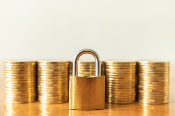 Money and Security Concept. Closeup of golden master key lock with stack of gold coins on wooden table.