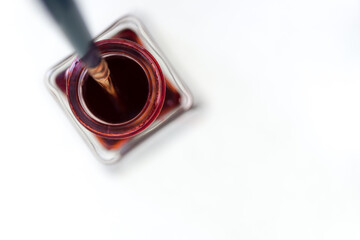 isolated deep red inkwell bottle - viewed from above with scripting paint brush - on white