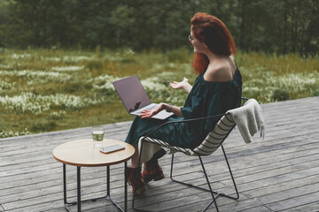 Back view of successful woman working with laptop and sitting outdoor in a beautiful terrace in forest