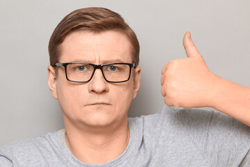 Portrait of serious man raising thumb up in approval gesture