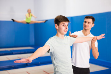 Obraz na płótnie Canvas Skilled coach holding training with teenager in trampoline room, explaining basic jumping tricks..