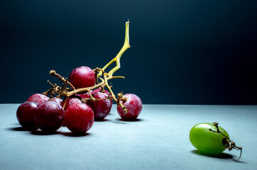 Racimo de uvas rojas y una uva verde asilada, idea de diferente, rechazo por ser diferente - obrazy, fototapety, plakaty