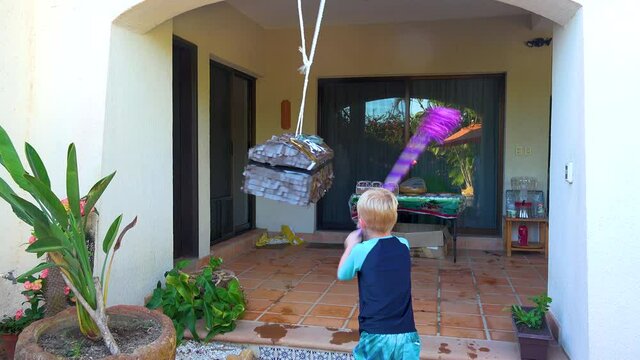 SAN JOSE DEL CABO BCS MEXICO-2020: Child Trying To Break Open A Pinata Hanging And An Adult Walks By In Front Of The Camera