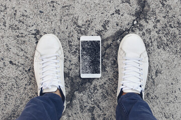 A smartphone falls on the street between the shoes of its owner just after being dropped.