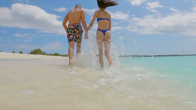 Back view of couple in swimwear holding hands running on beach, Dominican Republic. Slow-motion