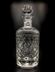 Empty crystal decanter with engraving, Closed with a glass stopper on black background. Selective...