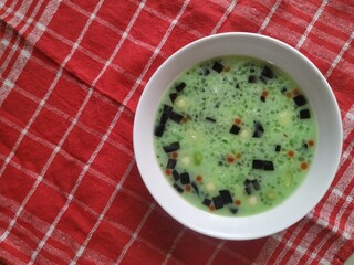 Es Campur. Icy Southeast dessert of fruits, jelly bubbles, noodle jelly, and basil seeds in sweet green syrup and milk soup on red towel background