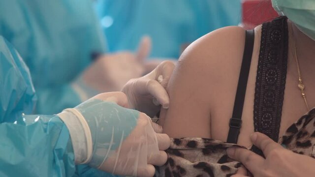 Medical Nurse in Safety Gloves and Protective Mask injects a dose of vaccine into the arm of Female Patient. Doctor Uses Hypodermic Needle and a Syringe to Put a Shot of Drug as Treatment.