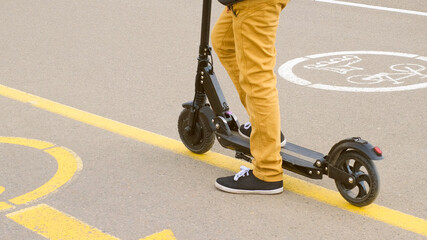 Back view of  legs of boy in yellow pants and black gumshoes on scooter. Close up