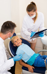 Male dentist with assistant are diagnosticating to young patient which is sitting in dental clinic.
