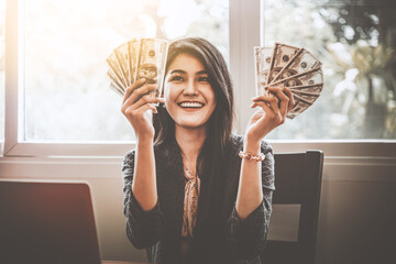Young happy businesswoman holding bills of dollars in office, happy excited successful.