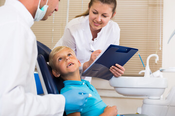 Obraz premium Dentist guy is diagnosing the child while female assistant is writing down patient's complaint in dental clinic.