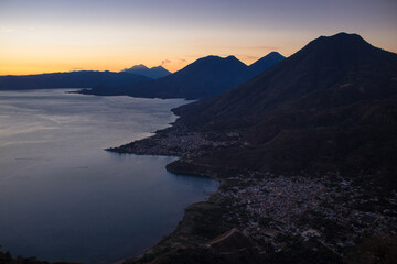 view from the viewpoint towards a town on the shore of a lake surrounded by volcanoes, mountains in the early hours of the morning with a beautiful cloudscape with warm tones