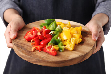 Chef holding chopped bell pepper in wooden cutting board on white background