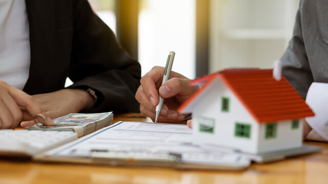 Real estate agents advise clients to rent or buy houses with contract documentation and laptop on their desk.