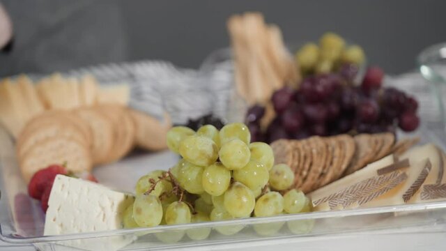 Step by step. Arranging cheese platter with fresh fruits, gourmet cheese, and crackers.