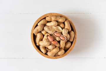 Top view of peanuts in a wooden bowl on white background,