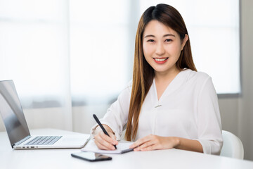 Young asian beautiful business woman working with laptop sitting at home and note on book. Smiling charming happy young female doing homework meeting conference with team at home.
