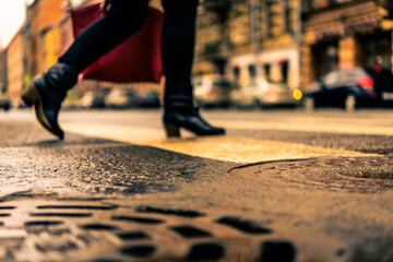 Rainy day in the big city, the woman with a red bag crosses the road on a pedestrian crossing. Close up view of a hatches at the level of the asphalt