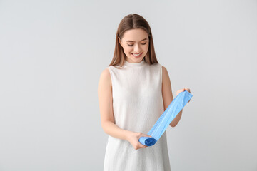 Young woman with garbage bags on light background