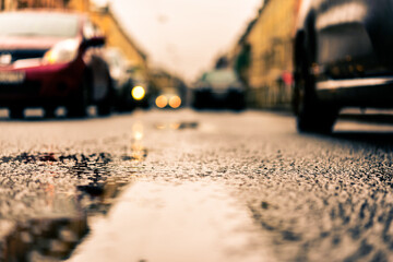 Rainy day in the big city, the cars drive along the road. Close up view from the level of the puddle on the pavement