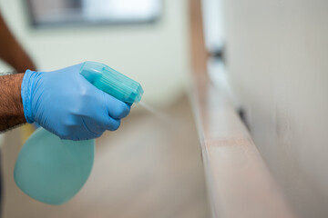 A young man cleans the stair handrail by spraying a cleaner to kill germs and viruses for good hygiene. He put on rubber gloves and wipes.