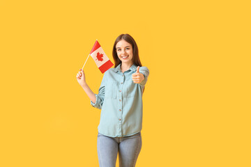 Beautiful young woman with the flag of Canada showing thumb-up on color background
