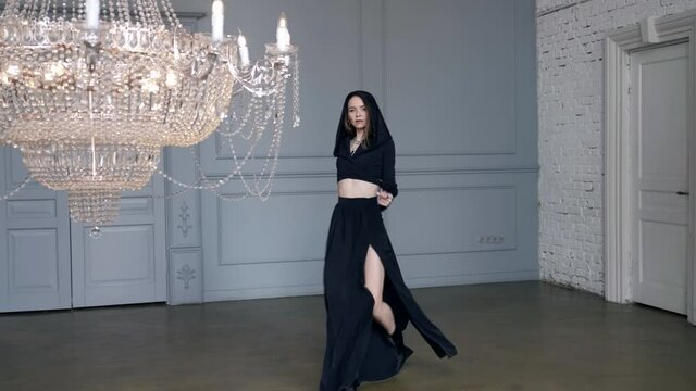 dramatic woman is dressed black gown, moving in light hall with luxury chandelier