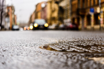 Rainy day in the big city, the headlights of the approaching cars. Close up view of a hatch at the level of the asphalt