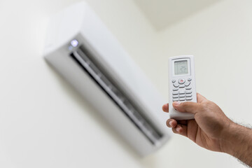 Fototapeta premium The young man used remote turn on the air conditioning . Adjust the temperature to cool. In the living room at home