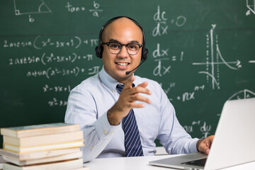 Indian young teacher man sitting wearing headset teaching online video conference live stream by laptop. Asian teacher teaching mathematics class webinar online for students learning.