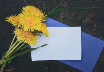 Bunch of dandelions on wooden background and a piece of paper for notes.
