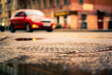 Rainy day in the big city, the red car is at the crossroads. Close up view of a hatch at the level of the asphalt