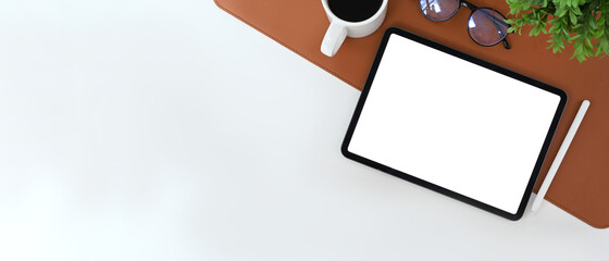 Minimal workspace with digital tablet, stylus pen, coffee cup and houseplant on white desk.
