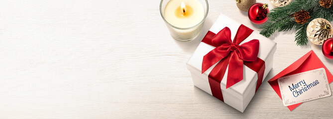 白木のテーブルの上に置かれたクリスマスプレゼントの箱、メッセージカード、キャンドル、クリスマスオーナメント。