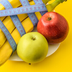 Yellow and red apples, ripe bananas wrapped in a centimeter, on a white plate, on a yellow background. Fitness, diet, weight loss concept. Copy space, selective focus.