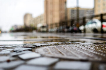 Rainy day in the big city, an empty road. Close up view of a hatch at the level of the asphalt