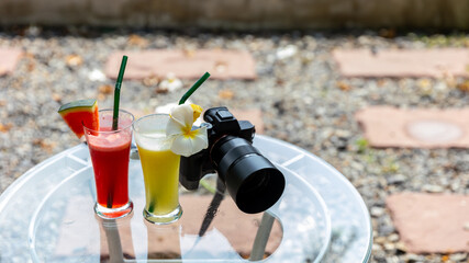 Two tasty colorful cocktail drinks next to a camera on a garden table ready for travelers during a pleasure vacation.