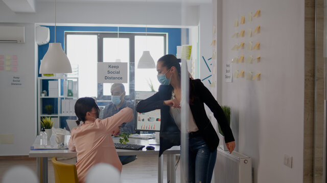 Coworkers touching elbow to avoid infection with coronavirus, business team wearing medical face mask while sitting on table desk working on company project respecting social distance