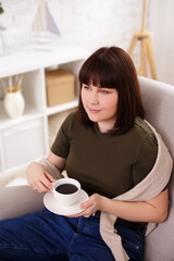 portrait of woman sitting on armchair and drinking coffee