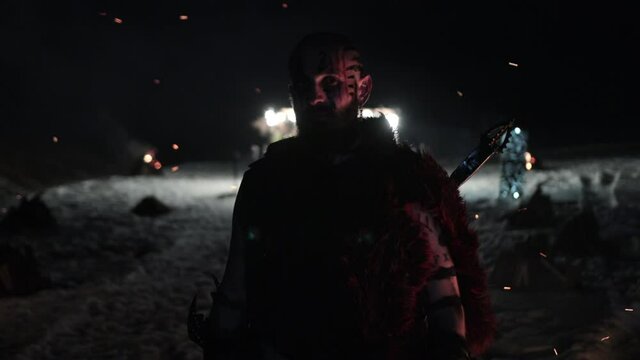 Viking is a brutal male warrior of dangerous appearance waiting for the enemy near fire. Concept of ancient traditions wild life barbarian conquerors. Low lighting, night.