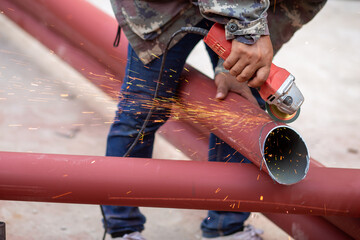Construction workers are using grinding machines on large steel pipes. Used as a roof pole. Sparking while working Red painted steel pipe To prevent rust and look beautiful