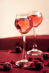 a glass of pink gin or vodka infused with cranberry among frozen berries, cherry liqueur or any red alcoholic cocktail closeup, a pair of long-stemmed glasses