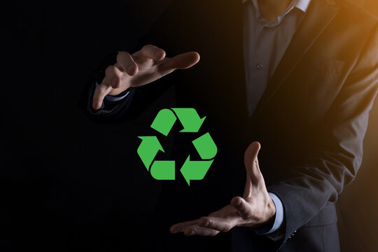 Businessman in suit over dark background holds an recycling icon, sign in his hands. Ecology, environment and conservation concept. Neon red blue light