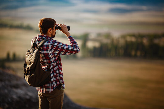 Guy looking at binoculars in hill. man in t-shirt with backpack.